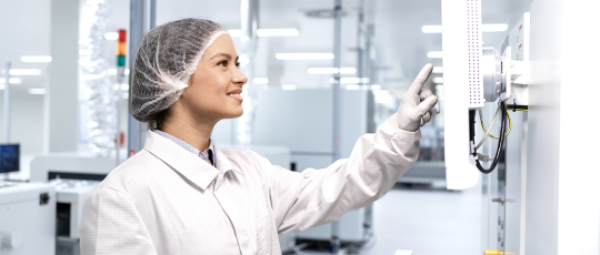 A woman in a clean suit works in a manufacturing facility 